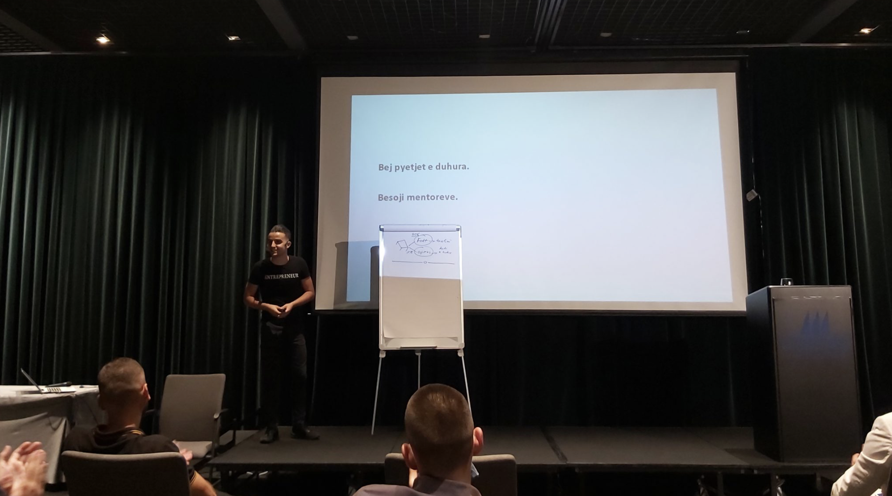 Dario Hani presenting on stage in front of a projector screen